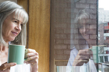 Frau mit Tasse, die durch ein Fenster schaut - CUF20065