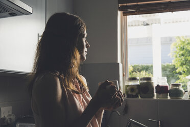 Young woman having a coffee break gazing through kitchen window - CUF20074