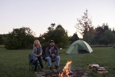 Father and daughter sitting beside campfire, toasting marshmallows over fire - ISF07472
