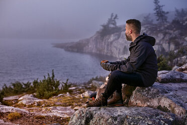 Wanderer entspannt mit Kaffee auf einer Klippe, Sarkitunturi, Lappland, Finnland - CUF20102