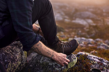 Hiker tying shoelace on rocky field, Sarkitunturi, Lapland, Finland - CUF20104