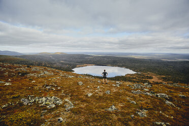 Trail runner looking at view on rocky cliff top, Keimiotunturi, Lapland, Finland - CUF20112