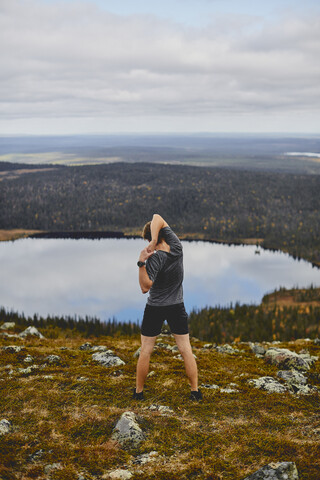 Man stretching on rocky cliff top, Keimiotunturi, Lapland, Finland stock photo