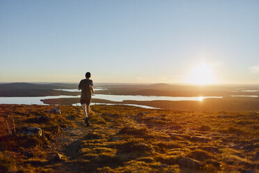 Mann beim Trailrunning auf einer Klippe bei Sonnenuntergang, Keimiotunturi, Lappland, Finnland - CUF20118