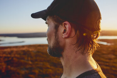 Man looking out to lake on cliff top at sunset, Keimiotunturi, Lapland, Finland - CUF20134