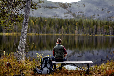 Wanderer ruht sich auf einer Bank aus und schaut auf einen See, Kesankijarvi, Lappland, Finnland - CUF20142