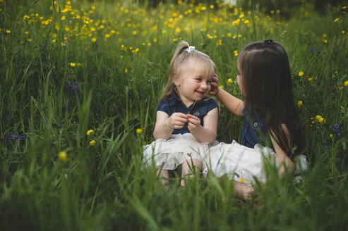 Mädchen sitzen auf einer Wildblumenwiese und lächeln sich an - CUF20148