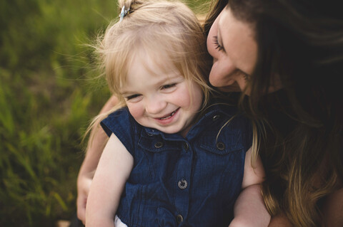 Mutter, die ein lächelndes Mädchen umarmt, lizenzfreies Stockfoto
