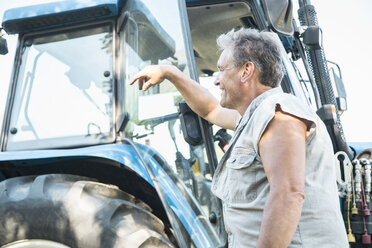 Älterer männlicher Landarbeiter lehnt sich an einen Traktor - CUF20157