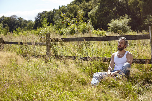 Mittlerer erwachsener Mann, der an einem ländlichen Zaun sitzt und starrt - CUF20165