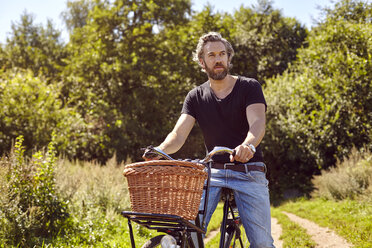 Mid adult man on bicycle gazing from rural dirt track - CUF20166