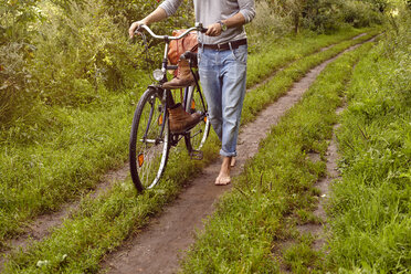 Neck down view of man pushing bicycle on rural dirt track - CUF20168