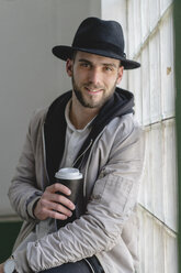 Smiling bearded man wearing black hat, holding coffee to go - AFVF00592