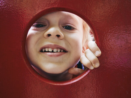 Portrait of smiling little boy looking through hole on playground - MUF01540