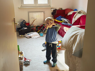 Kleiner Junge steht in seinem unordentlichen Zimmer und macht ein Kreuz mit seinen Fingern - MUF01554