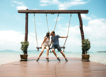 Thailand, Koh Lanta, kissing couple sitting on swings in front of the sea - GEMF02049