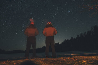 Sweden, Sodermanland, two men standing at lakeside under starry sky at night - GUSF00915