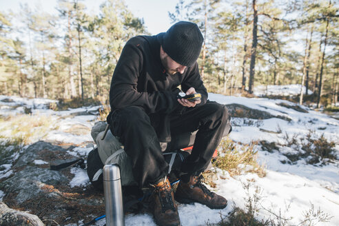 Schweden, Sodermanland, Rucksacktourist rastet in abgelegener Landschaft im Winter mit GPS-Tracker - GUSF00928