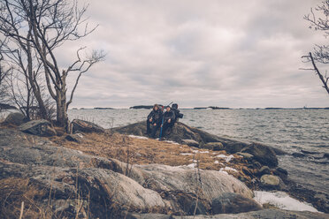 Sweden, Sodermanland, two men resting at the seashore under cloudy sky - GUSF00936