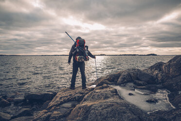 Sweden, Sodermanland, backpacker standing at the seashore under cloudy sky - GUSF00937