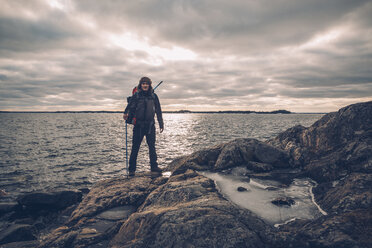Sweden, Sodermanland, backpacker standing at the seashore under cloudy sky - GUSF00938
