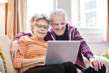 Älteres Paar auf dem Wohnzimmersofa mit Blick auf den Laptop - CUF20279
