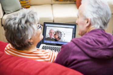 Blick über die Schulter auf ein älteres Ehepaar auf dem Wohnzimmersofa, das sich Fotos auf einem Laptop ansieht - CUF20280