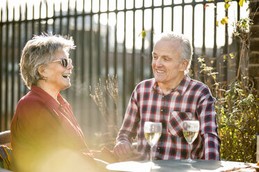 Senior couple on rooftop garden chatting and relaxing with white wine - CUF20281