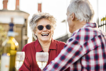 Senior couple on city rooftop garden chatting and relaxing with white wine - CUF20282