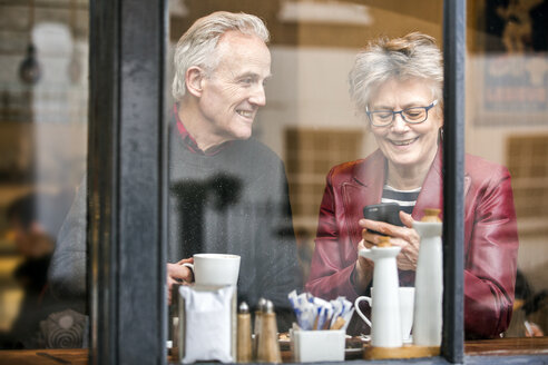 Älteres Ehepaar auf dem Fensterplatz eines Cafés trinkt Kaffee und schreibt eine SMS auf dem Smartphone - CUF20285
