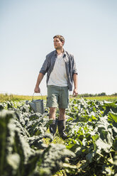 Man in vegetable garden carrying watering can, looking away - CUF20301