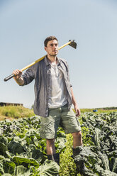 Mann im Gemüsegarten, der eine Hacke auf der Schulter trägt und wegschaut - CUF20304
