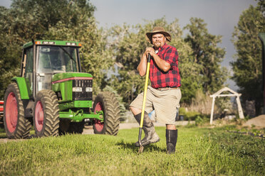 Landwirt vor einem Traktor, der sich gegen eine Hacke lehnt und lächelnd in die Kamera schaut - CUF20324