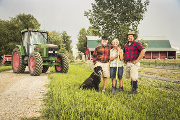 Familie mit Hund auf einem Bauernhof vor einem Traktor schaut lächelnd in die Kamera - CUF20331