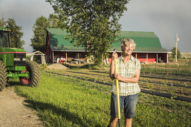 Frau auf einem Bauernhof neben einem Traktor, der lächelnd wegschaut - CUF20333