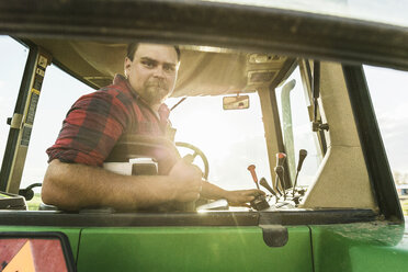 Farmer in tractor looking over shoulder out of rear window at camera - CUF20339