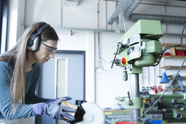 Seitenansicht einer Frau in einer Werkstatt mit Gehörschutz bei der Arbeit mit einer Bandschleifmaschine - CUF20343