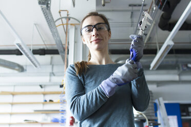 Niedriger Blickwinkel auf eine Frau in einer Werkstatt, die eine Schutzbrille trägt und ein Werkzeug hält - CUF20346