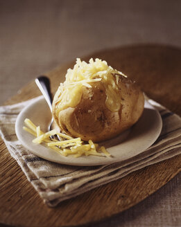 Gebackene Kartoffel mit geriebenem Cheddar-Käse auf Holzbrettchen - CUF20371