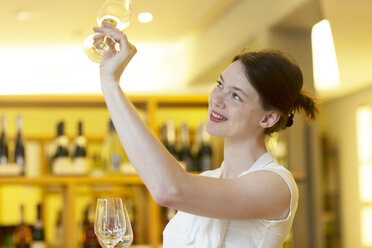 Frau im Weinladen hält Weinglas hoch und prüft Sauberkeit - CUF20398