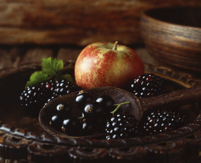 Apple, blackberries and blackcurrants in vintage wooden bowl with wooden spoon, close-up - CUF20430