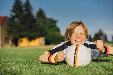 Junge im deutschen Fußballtrikot liegt auf dem Rasen und drückt die Daumen für die Weltmeisterschaft - MJF02314