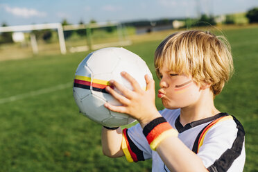 Junge mit Gesichtsbemalung und deutschem Fußballtrikot, der einen Fußball küsst - MJF02315