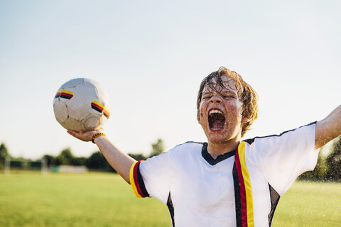 Junge mit deutschem Fußballtrikot, der vor Freude schreit und in Wasserspritzern steht, lizenzfreies Stockfoto