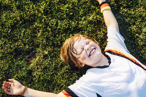 Junge in deutschem Fußballtrikot liegt lachend im Gras, lizenzfreies Stockfoto