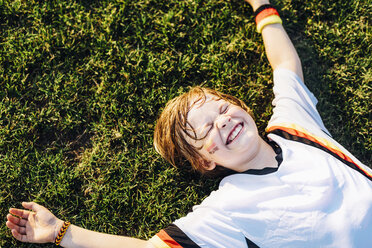 Boy in German soccer shirt lying on grass, laughimg - MJF02349