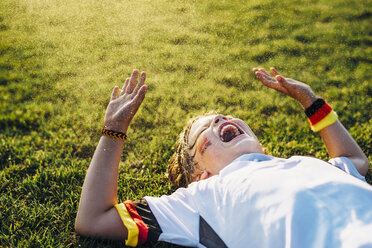 Boy in German soccer shirt lying on grass, laughing and screaming - MJF02350