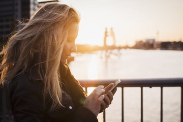 Frau benutzt Mobiltelefon bei Sonnenuntergang, Spree, Berlin, Deutschland - CUF20453