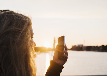 Woman taking photograph at sunset, Spree River, Berlin, Germany - CUF20454