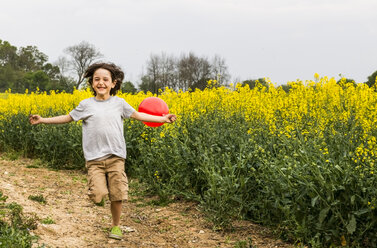 Boy running on yellow flower field track pulling red balloon - CUF20456